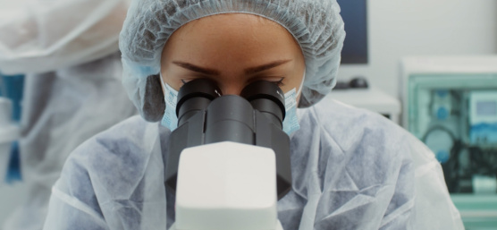 A person wearing a protective suit is looking through a microscope
