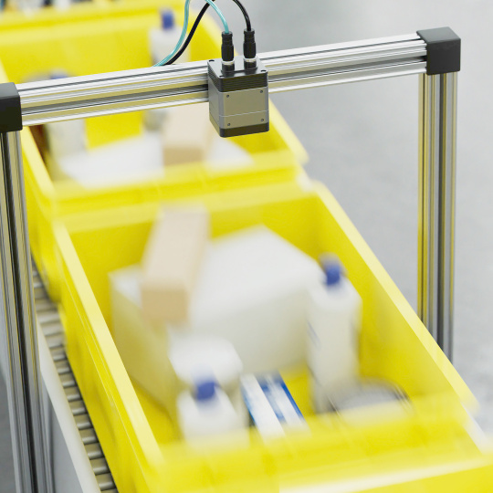 Industrial camera above yellow crates on a conveyor.