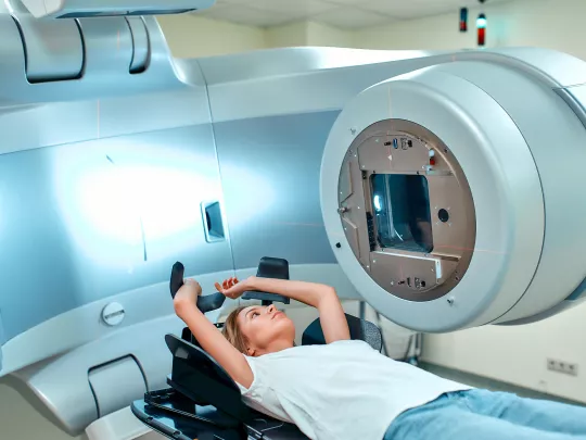 A woman lies on a medical couch in front of a radiotherapy machine