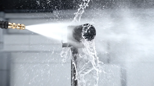 An industrial camera is sprayed with a powerful jet of water from close range.