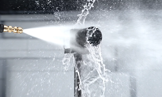 An industrial camera is sprayed with a powerful jet of water from close range.