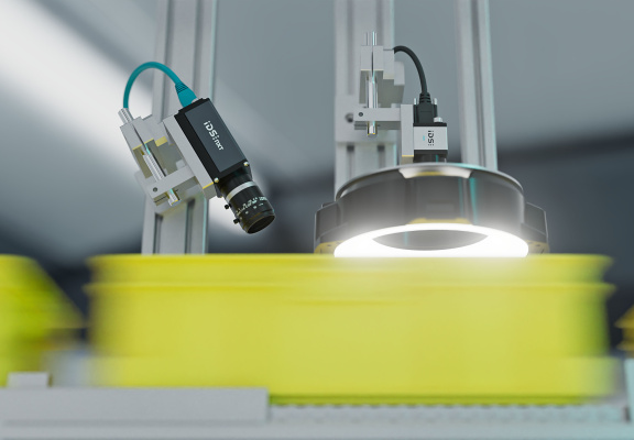 An industrial camera with a lens and LED ring light inspects yellow bulk material