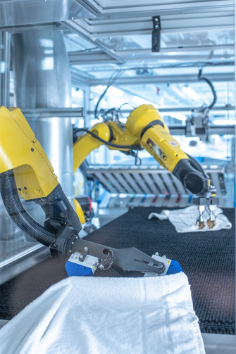 Two robots unfold laundry in a industrial laundry with the help of IDS 2D and 3D cameras.