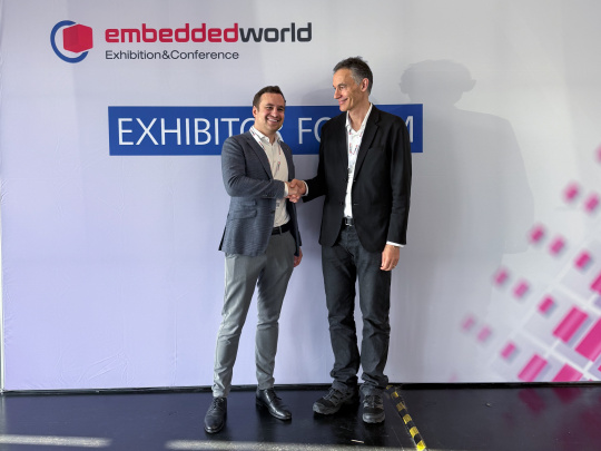Two managing directors shake hands in front of an Embedded World exhibition wall