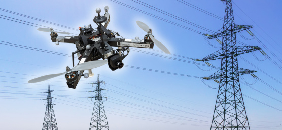 A drone with IDS camera hovers in front of power lines and three electricity pylons.