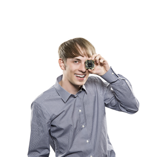 A man stands laughing in front of a white background and covers one of his eyes with a board camera.