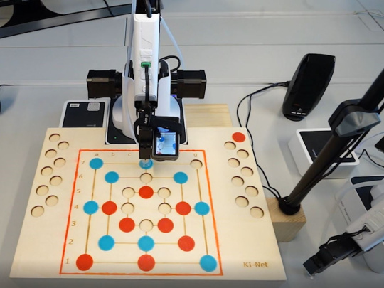 Robot arm with camera in front of mill game board