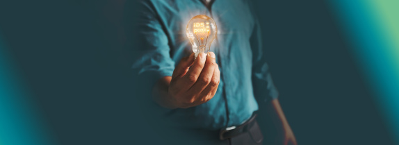 Person holding illuminated “iDS peak” light bulb against dark background