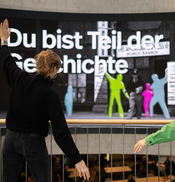 Two people are posing in front of a large interactive display wall featuring coloured silhouettes