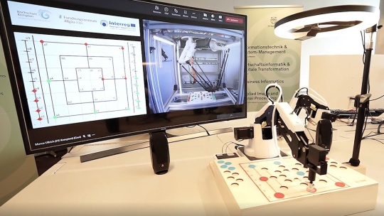 Robot plays mill on the game board and is illuminated by a lamp, screen next to it
