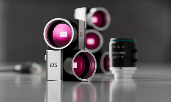 uEye CP cameras stacked, a lens next to them, grey, reflective background