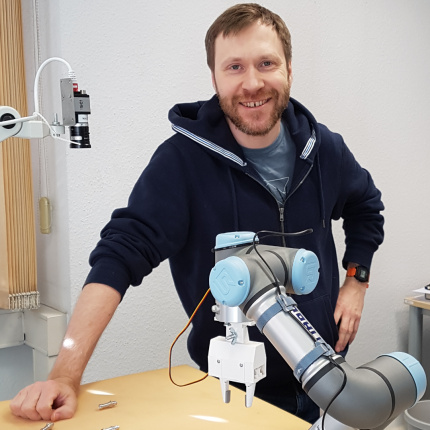 Speaker Alexey Pavlov next to robotic arm and IDS uEye camera