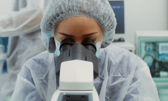 A person wearing a protective suit is looking through a microscope